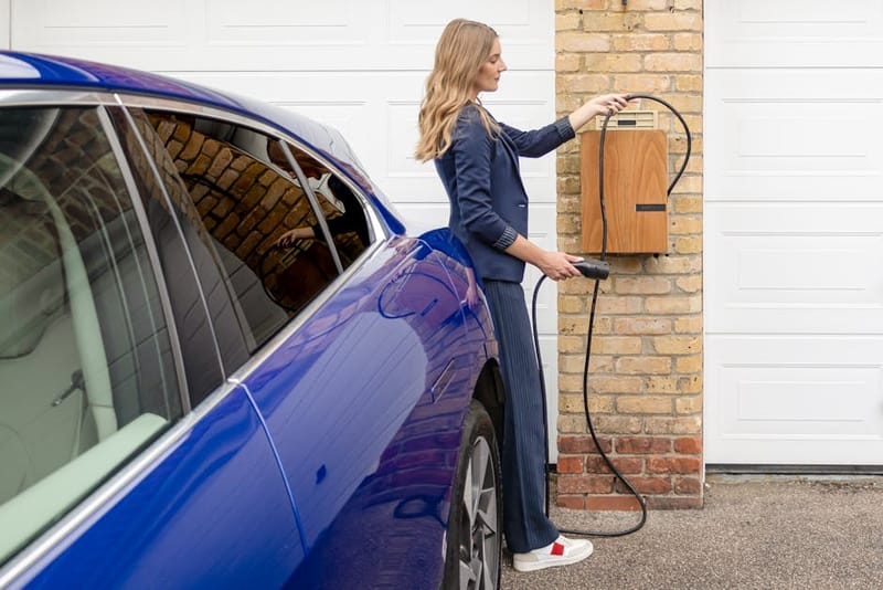 Person plugging in an EV charger at a home charging station — installations like this qualify for the £500 OZEV grant from 1 April 2026